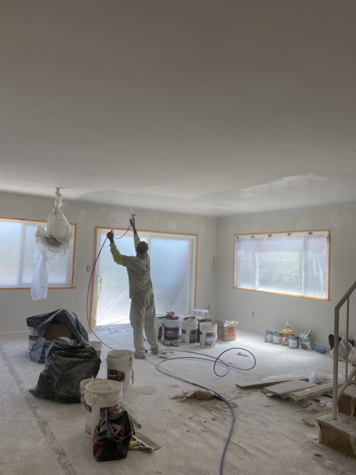 a worker painting the ceiling of the house with white paint