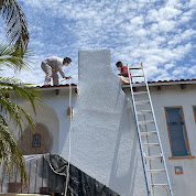 two workers standing on the roof  painting the high end of the wall of the house