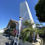 An image of a worker painting the wall of the square tower beside the house