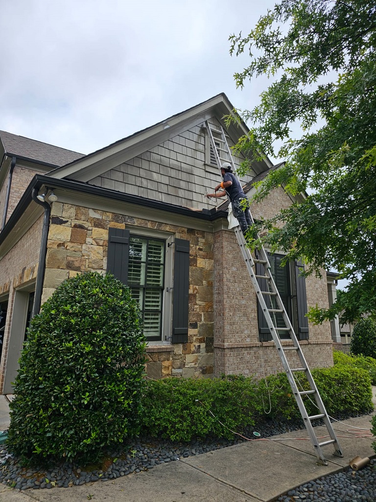 A picture of a worker standing on the ladder painting the exterior wall of the house